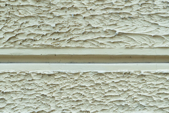 ​Horizontal close up photo of textured rough white plaster wall facade divided by central horizontal recessed architectural groove line for masonry background