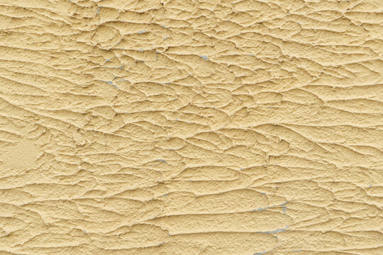 ​Horizontal close up photo of rough yellow stucco wall plaster texture with textured trowel relief pattern for decorative masonry surface background design