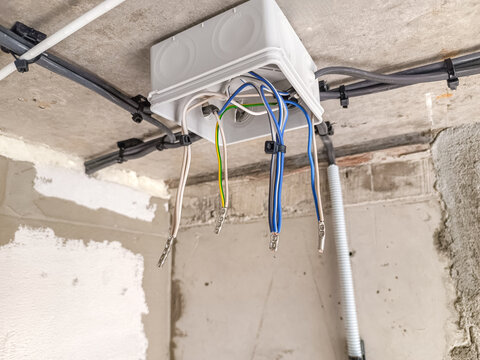 Electrical junction box with multiple colored wires attached to the ceiling. The setting is an unfinished room with exposed walls and ceiling.