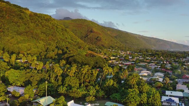 Drone flight over Moorea island vibrant tropical village nestled along the coastline, surrounded by lush green mountains and abundant palm trees under a bright sky. Rural landscape in French Polynesia