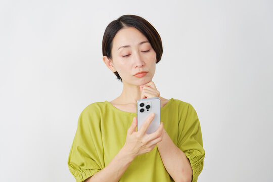 スマホを持って考えるミドル女性　白背景