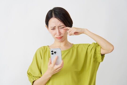 スマホを持って泣くミドル女性　白背景