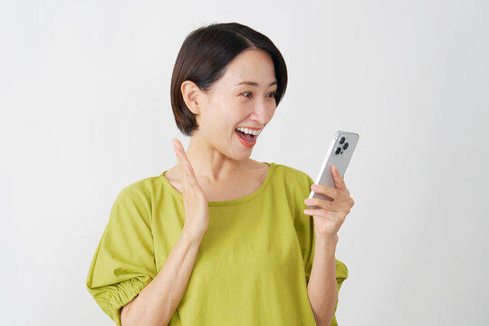 スマホを持って笑顔で驚くミドル女性　白背景