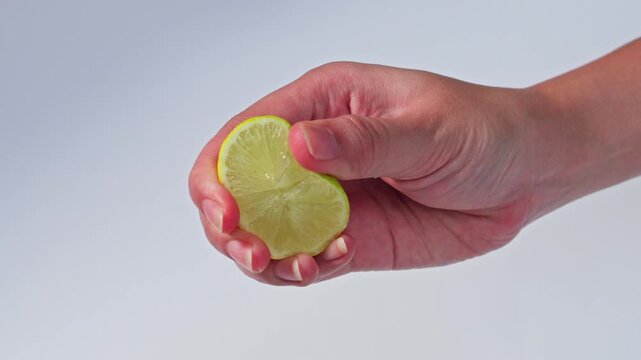 Slow-motion close-up of hand squeezing fresh lime juice against clean white backdrop