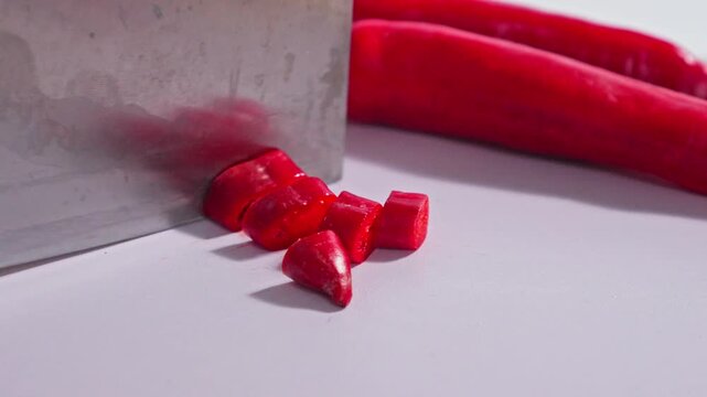 Close-up of red chili pepper pieces being sliced with heavy cleaver blade