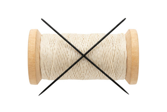 Eine h&ouml;lzerne Garnrolle mit beigem N&auml;hgarn, die von zwei gekreuzten schwarzen Stricknadeln auf einem sauberen, wei&szlig;en Hintergrund durchgestrichen oder markiert wird, isoliertes Studio-Foto.