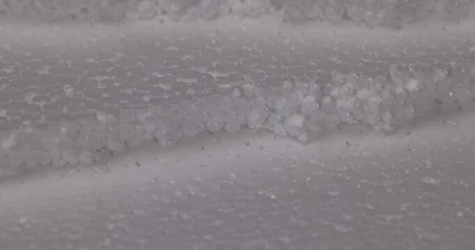 Granular white foam with bends, multilayer foam has a porous structure and alternating light and dark stripes on the surface.