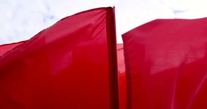 Fluttering red flags on the flagpole, a group of red flags fluttering outdoors in windy weather with clouds