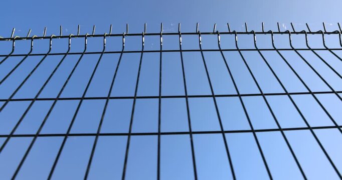 Black welded mesh fence against empty blue sky, industrial wire fencing lattice at border of facility yard on clear sunny day