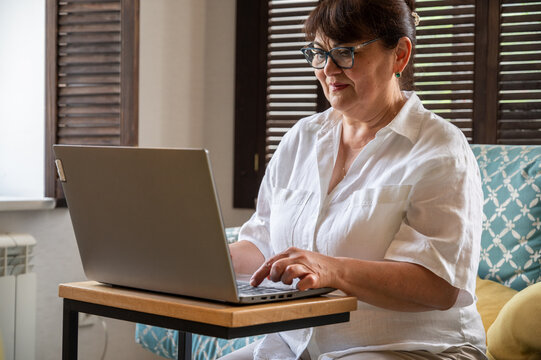 Senior woman wearing glasses and works on a laptop at home. Work from home, remote work, writing