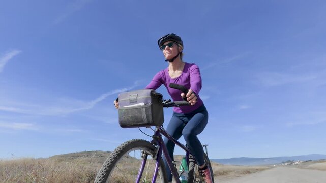 Mature woman enjoys biking along a paved trail in Fort Bragg near Mendocino California on a clear sunny day next to the ocean.