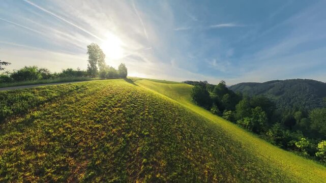 Drone footage following a rural road and green meadow while slowly ascending toward the morning sun over the M&uuml;hlviertel. Low clouds linger above forests and fields in Upper Austria.