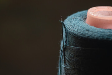 Obraz premium Macro close-up of a steel sewing needle with threaded fiber inserted in a teal thread spool