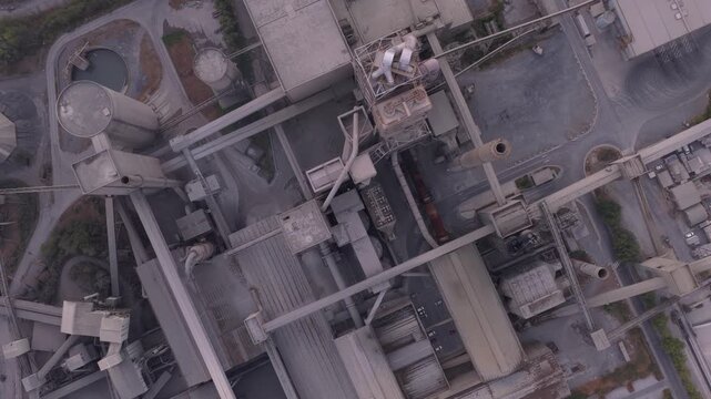 Drone's perspective flying over an industrial zone with a cement plant. Complex structures, silos, and conveyors for material processing