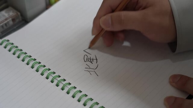 Hand writing Japanese characters with a wooden pencil in a spiral bound notebook