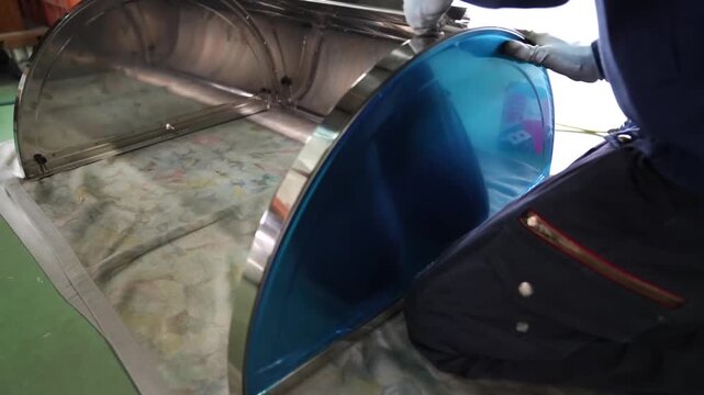 Worker bending blue coated metal sheet into curved cone shape on wooden mold