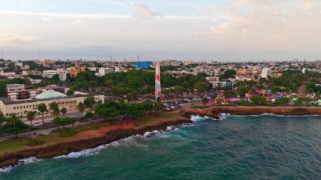 Daytime aerial drone shot tracking right over Caribbean Sea waves along Santo Domingo Malecon, featuring the Obelisco Macho monument and Juan Baron par