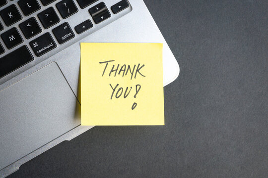 Handwritten Thank you on yellow note, on top of computer laptop. Top view.