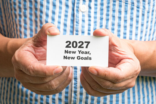 Man holding a white card with message, 2027 New Year New Goals. Close up view.