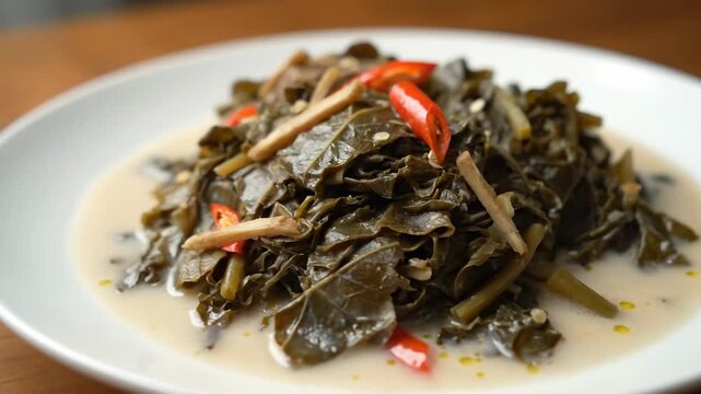 Traditional Indonesian Sayur Daun Singkong Tumbuk (Mashed Cassava Leaves) Cooked in Creamy Coconut Milk Sauce Garnished with Spicy Red Chili Peppers.
