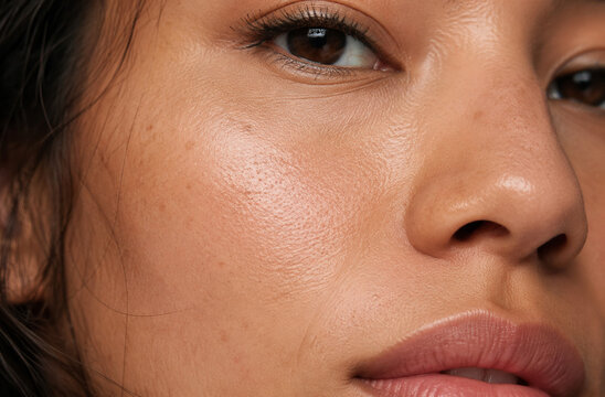 A close-up macro shot reveals the glowing, healthy skin of a young woman, highlighting her natural beauty with a subtle sheen.