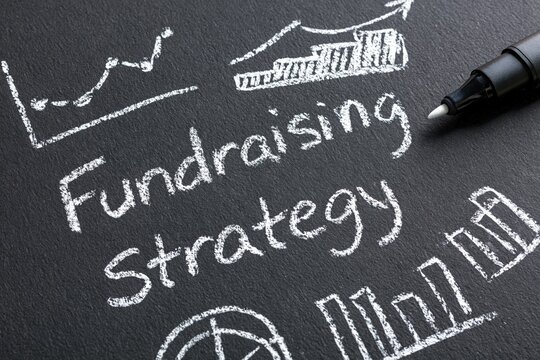 Fundraising strategy written in chalk on a black board with business finance charts and marketing growth planning