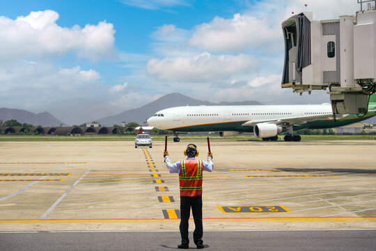 Aviation marshaller meets airplane at the airport. Travel by plane. Airplane flight. Adjuster, the regulator on the runway meets the plane. Airport worker, modern airport, aviation business