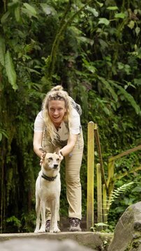 Blonde woman smiling and playing with a stray dog on a trail in the mindo cloud forest in ecuador