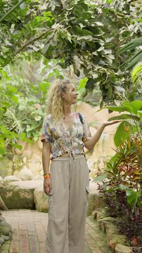 Blonde woman smiling in a lush tropical garden while holding a butterfly on her hand in mindo, ecuador