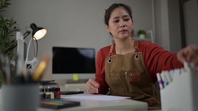 Focused asian artist drawing with colorful markers at her desk. 3d printer