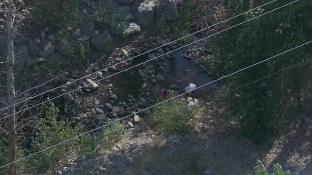 Two homeless individuals leaning over rocks in a rocky creek