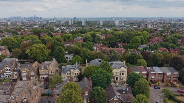 Leafy residential streets in North West London with large homes, apartment buildings, mature trees and the distant city skyline, aerial panning view