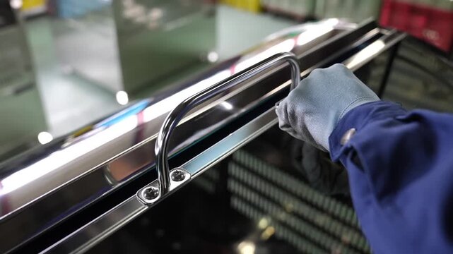 Worker installing handle bracket rail onto stainless steel bin lid in factory