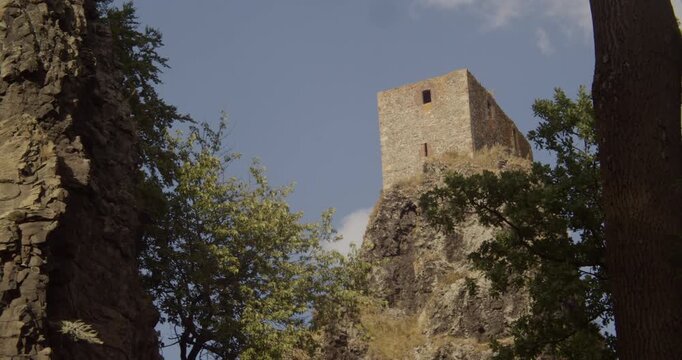 A low angle shot of the historic Trosky Castle tower perched on a volcanic rock formation, surrounded by lush green trees in the Bohemian Paradise region.
