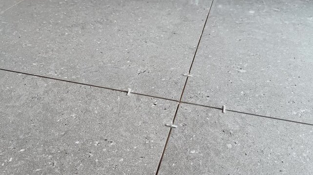 Close-up of a worker adjusting white spacers between large gray floor tiles, showing precise alignment and professional flooring installation during an interior renovation.