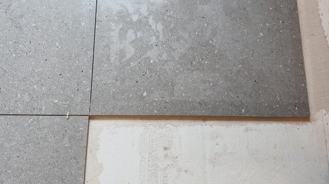 Close-up of a worker positioning a large gray floor tile beside spacers during an indoor renovation, showing precise alignment and hands-on ceramic installation.
