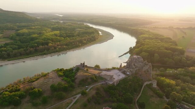 Spectacular aerial drone view of Devin Castle at golden hour overlooking the Danube and Morava rivers near Bratislava, Slovakia. Historic fortress surrounded by forests and scenic landscape.