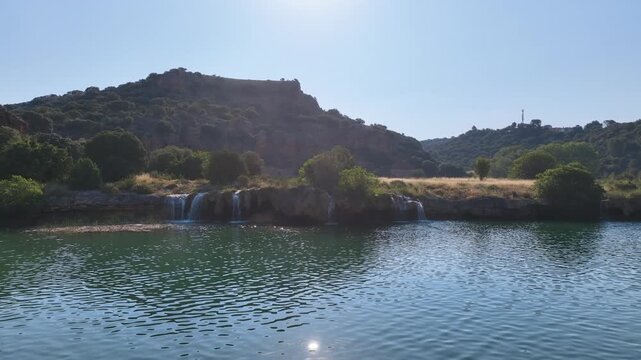 Flights quickly reverses from intimate rows of waterfalls under the powerful glare of low morning sun, and reveals lagoon and lush forest clad hills. Lagunas de Ruidera Spain.