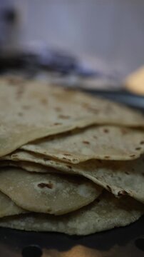 Close-up of freshly made chapatis stacked on a dark surface in a home kitchen. Thin, unleavened flatbread with charred spots, warm cream and brown tones, soft natural lighting, cozy domestic cooking a