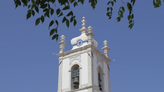 White bell tower and clock of the Igreja Matriz against blue sky in Sesimbra
