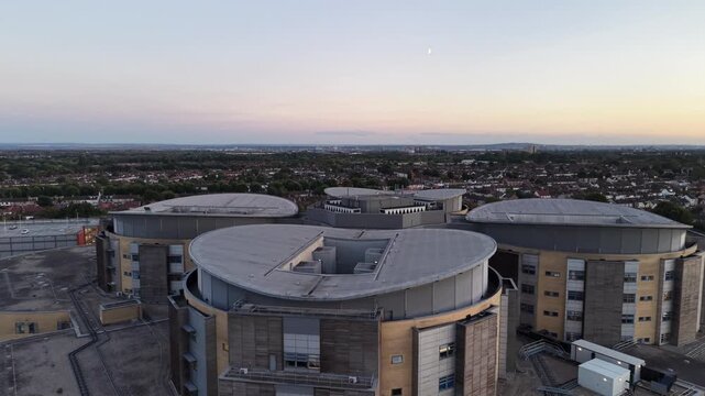 4K UHD drone pull-out shot flying backward to reveal the massive architecture of Queens Hospital in Romford, England. Soft golden hour lighting at the end of the day
