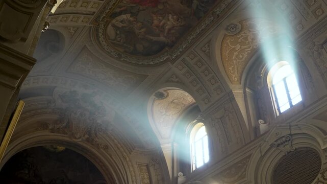 Bright shafts of sunlight stream through high windows, illuminating detailed baroque ceilings inside an old Rome church.