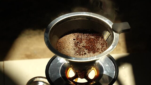 High-angle close-up of fresh coffee blooming and dripping through a stainless steel filter dripper.