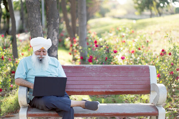 Fototapeta premium Indian senior sikh man working on laptop at park
