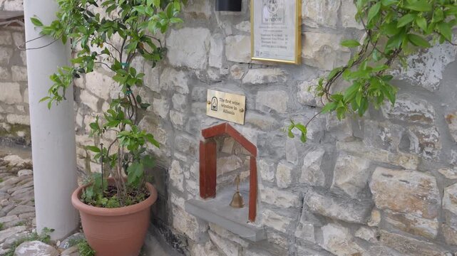 Wine Window brass plaque and framed sign on stone wall with climbing vine in Berat Albania