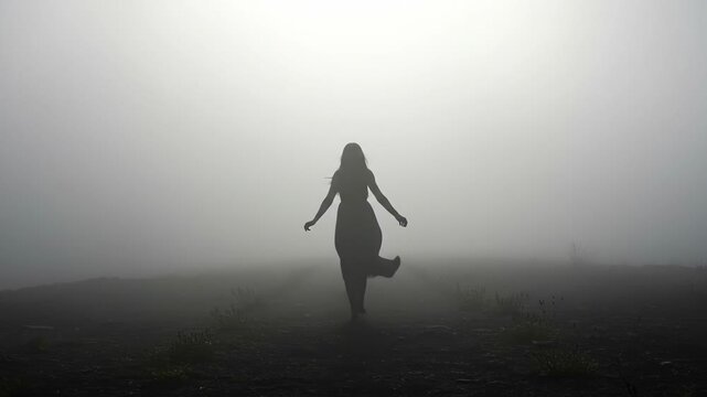 Mysterious silhouette of a woman walking alone through a thick, atmospheric fog.