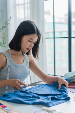 Asian woman tailor using scissors to cut off excess threads.