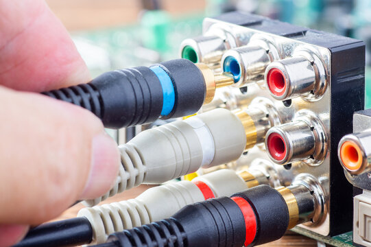 Hand plugging a blue RCA cable into an analog audio-video connector panel on a circuit board