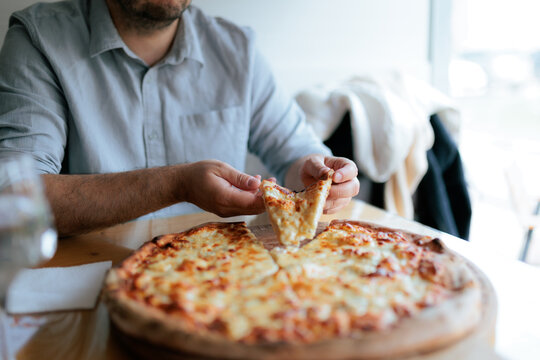 Hungry Man Hands Taking Hot Slice From Fresh Whole Pizza. Male person grabs cheesy Italian crust food sitting at restaurant indoor table
