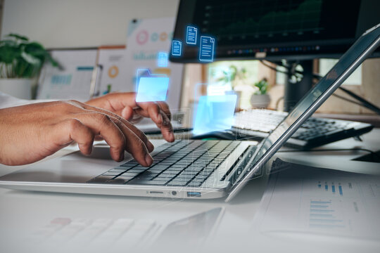 Business professional using laptop and digital hologram interface manage folders and files transfer, concept of electronic document management, data storage, cloud computing, and digital office.